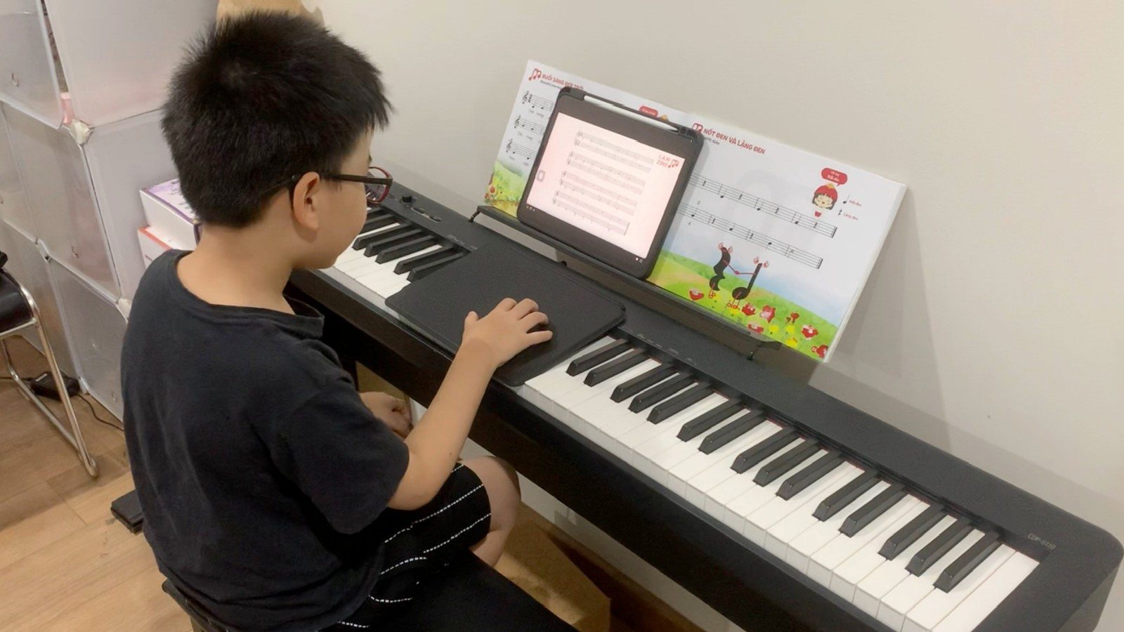 Bạn nhỏ tự ngồi vào đàn piano điện, xem bài học trên máy tính bảng tại nhà
